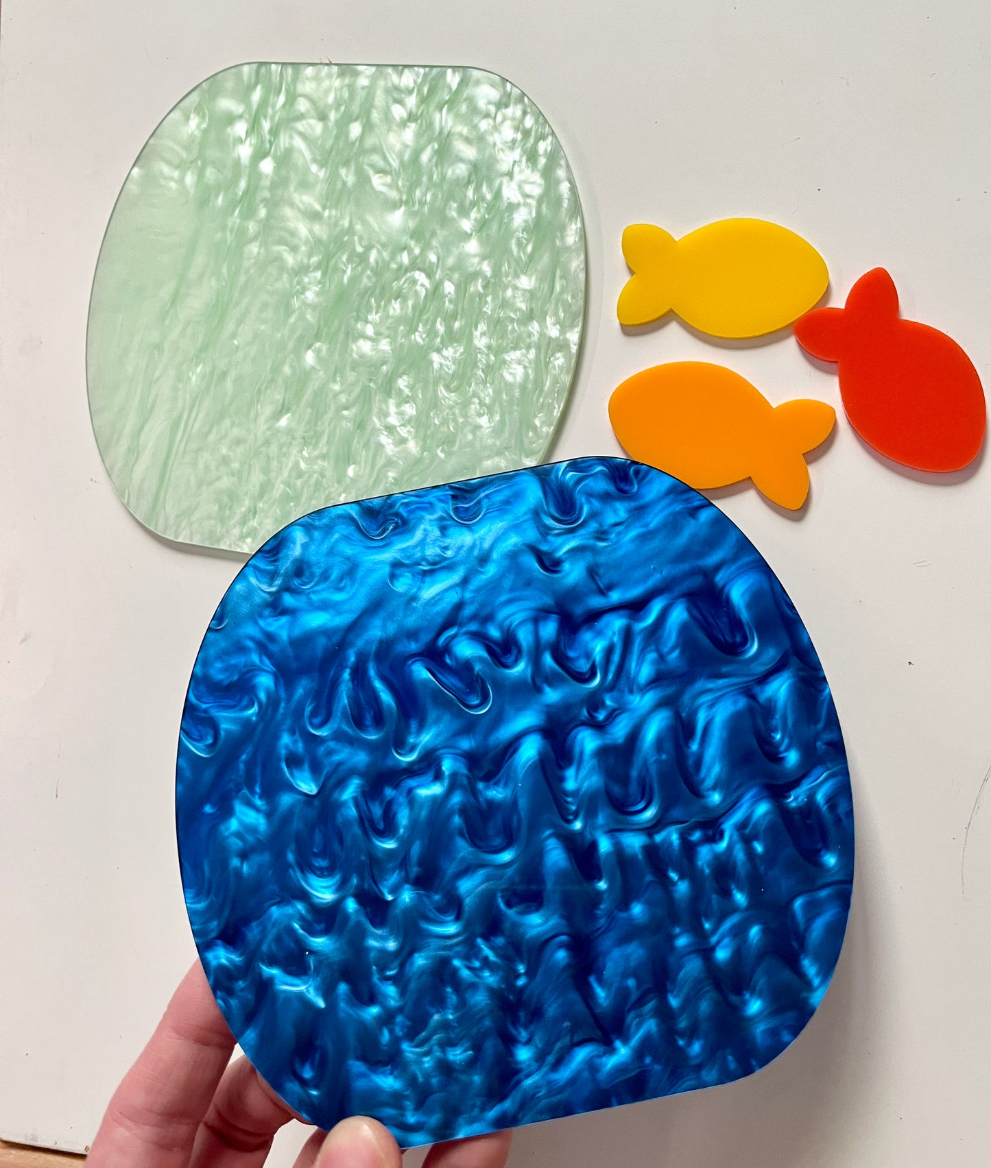 Blue marble dry erase pond held by a hand, with green, yellow, orange, and red fish-shaped objects on a white background.