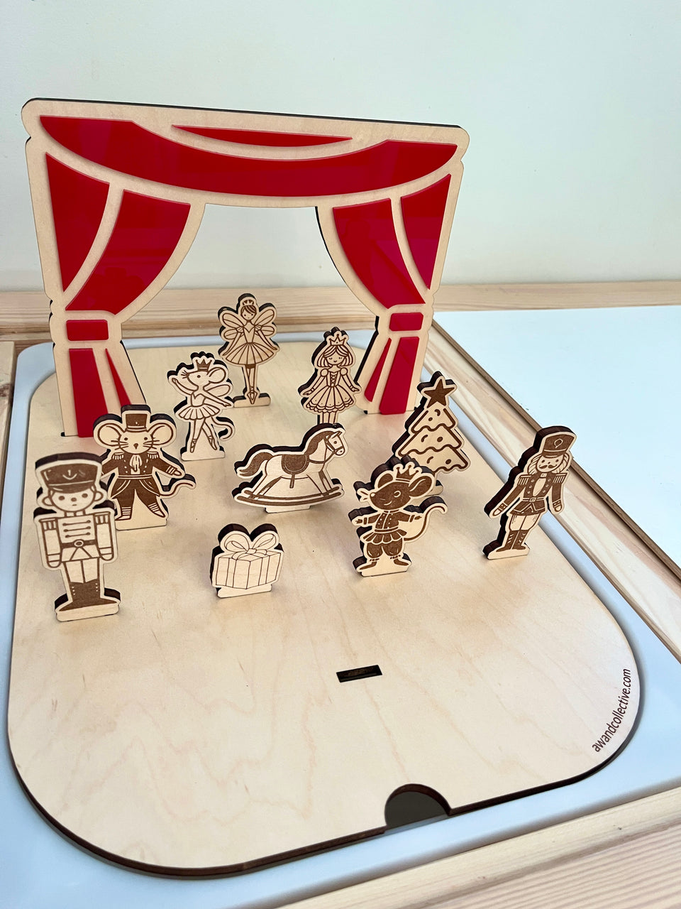 Wooden stage set with red curtains and engraved holiday-themed figurines including a nutcracker, ballerina, and Christmas tree
