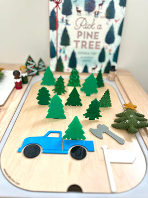 Wooden activity board featuring green tree shapes, blue truck, gray axe, white flag, and felt Christmas tree with star topper