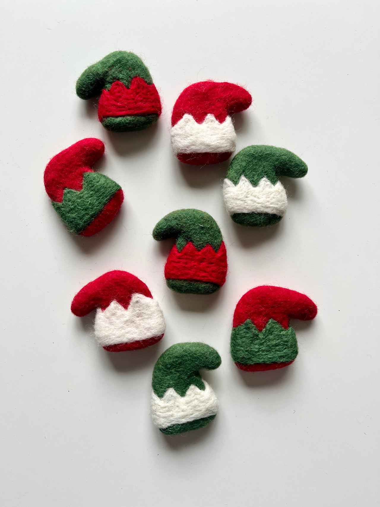Felt Christmas elf hats in red, green, and white with zigzag trim arranged on a white background