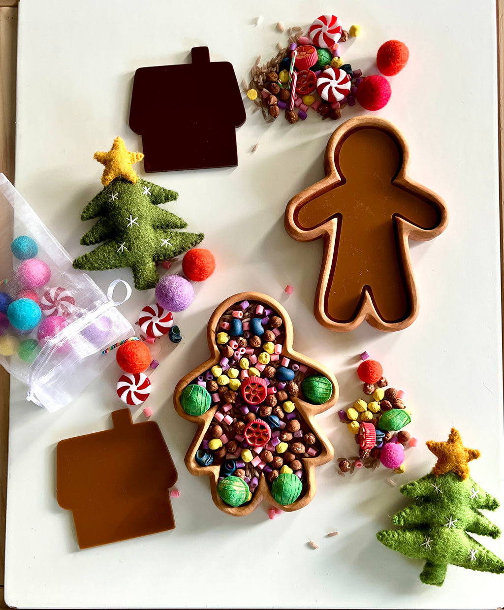 Gingerbread man and house-shaped trays with colorful beads, pom-poms, felt Christmas trees, and candy decorations scattered around