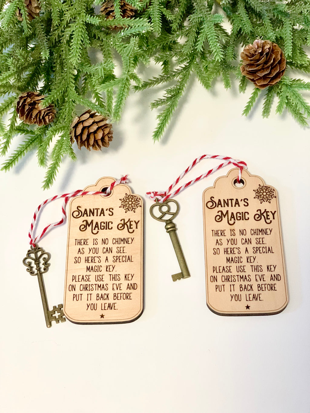 Two wooden tags engraved with Santa’s Magic Key poem alongside vintage-style metal keys and pine branches with cones on white surface