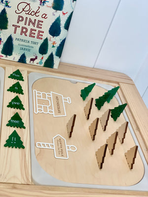 Wooden Flisat insert with 12 plantable Christmas trees in maple plywood and green acrylic beside pine tree book on wooden table