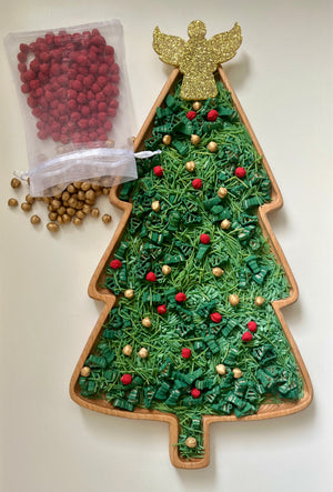 Christmas tree-shaped wooden tray filled with green shredded paper, red and gold decorative beads, and topped with a glittery gold angel