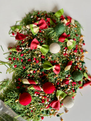 Close-up of colorful birdseed mix with green pine needles and red, white, and green festive decorations scattered on white surface
