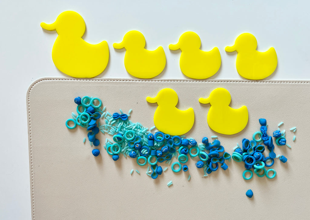 Yellow duck-shaped counters arranged in a row above scattered blue and teal plastic pieces on a beige surface