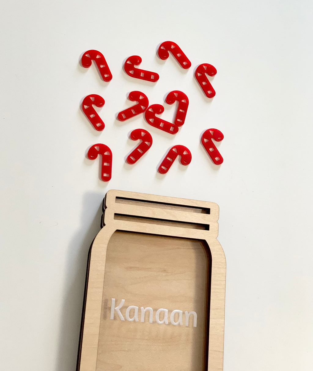 Natural wooden jar-shaped frame personalized with the name Kanaan and scattered red candy cane tokens on white background