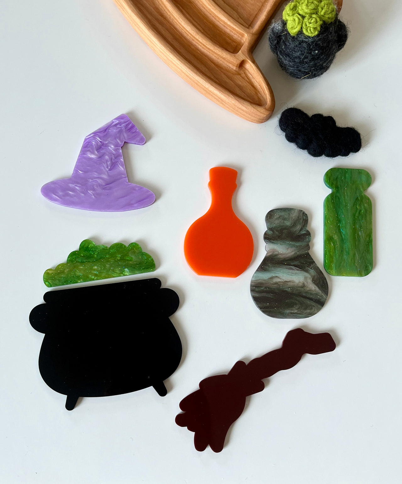 Assorted flat acrylic Halloween shapes including witch hat, cauldron, potion bottles, and broomstick on white surface