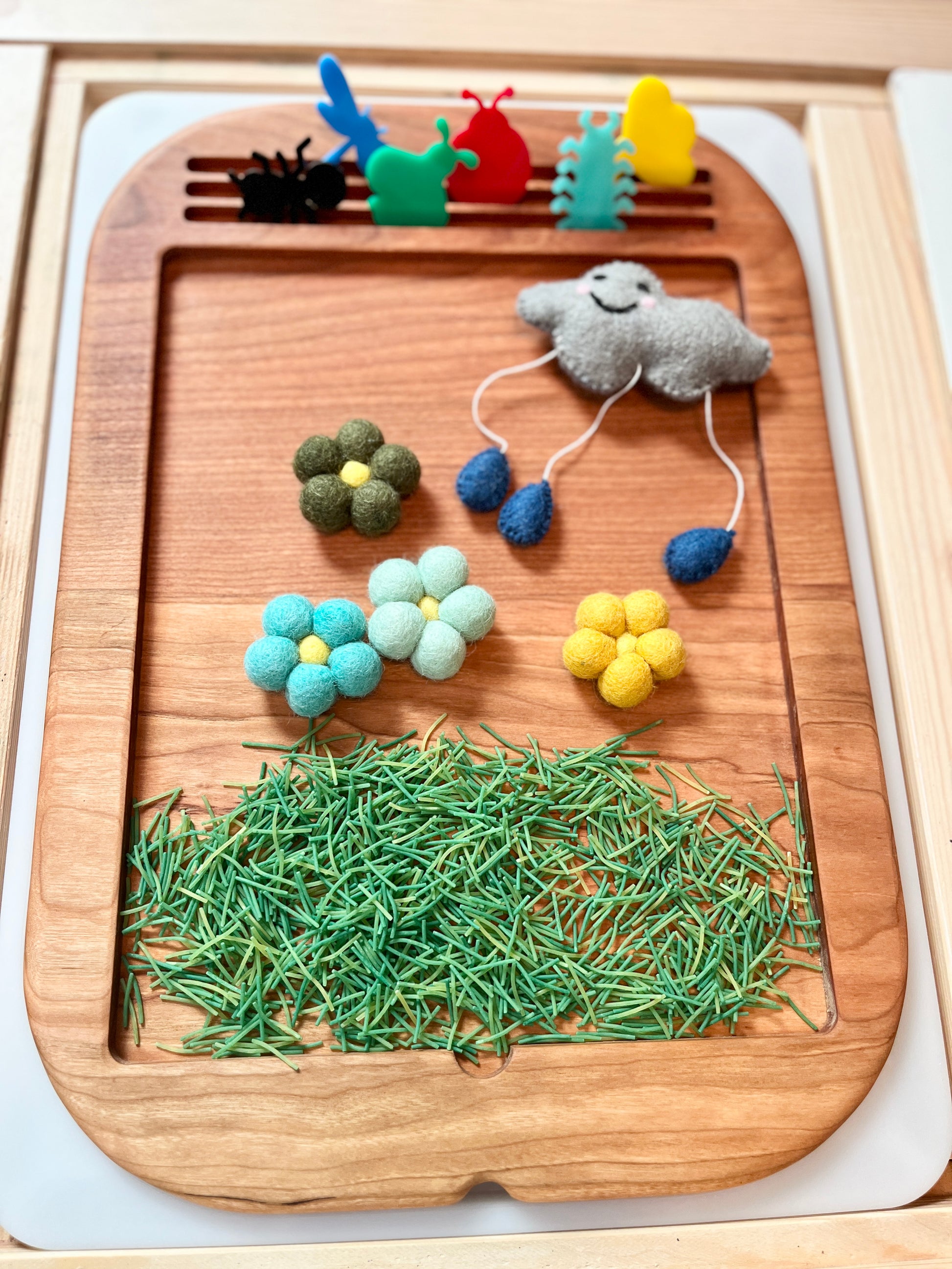 Wooden tray with felt toys, sensory filler and flowers on a flisat table