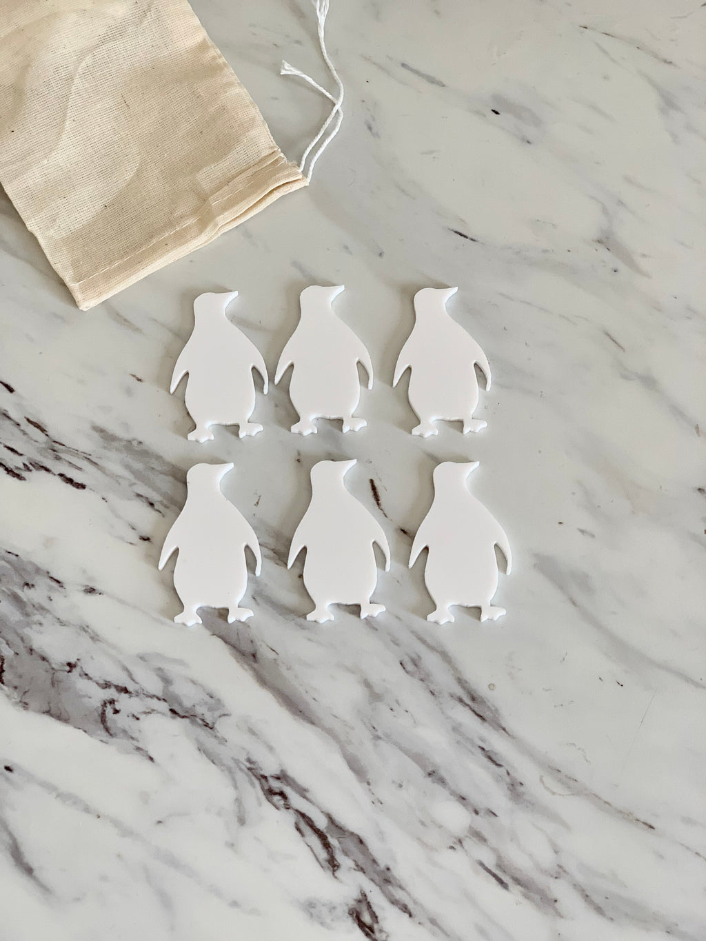 Set of six white penguin-shaped dry erasable boards with drawstring cotton pouch on marble surface