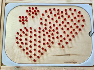 Wooden board with four heart outlines filled with removable red pegs on a light wood background.
