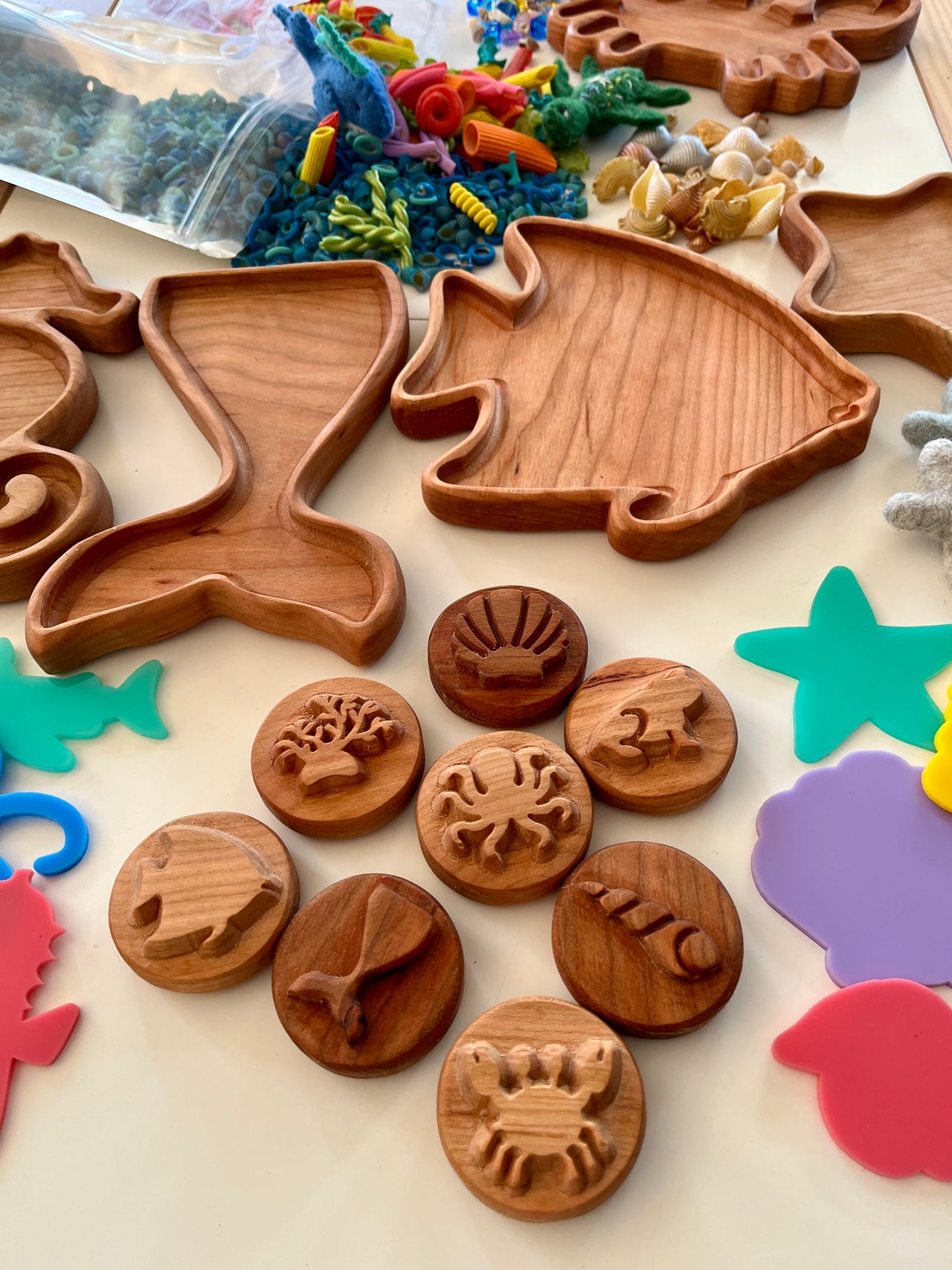 Wooden trays shaped like a seahorse and fish with round wooden sea creature stamps and colorful craft pieces on table
