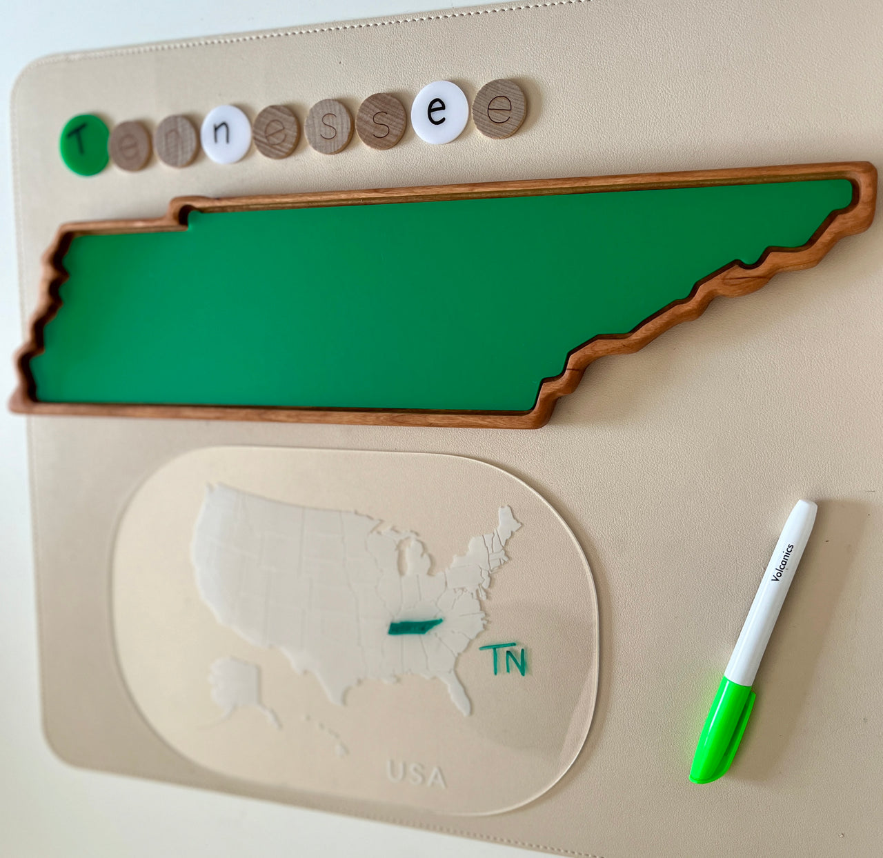 Green wooden tray shaped like Tennessee with letter tokens spelling Tennessee and a dry erase marker on beige surface