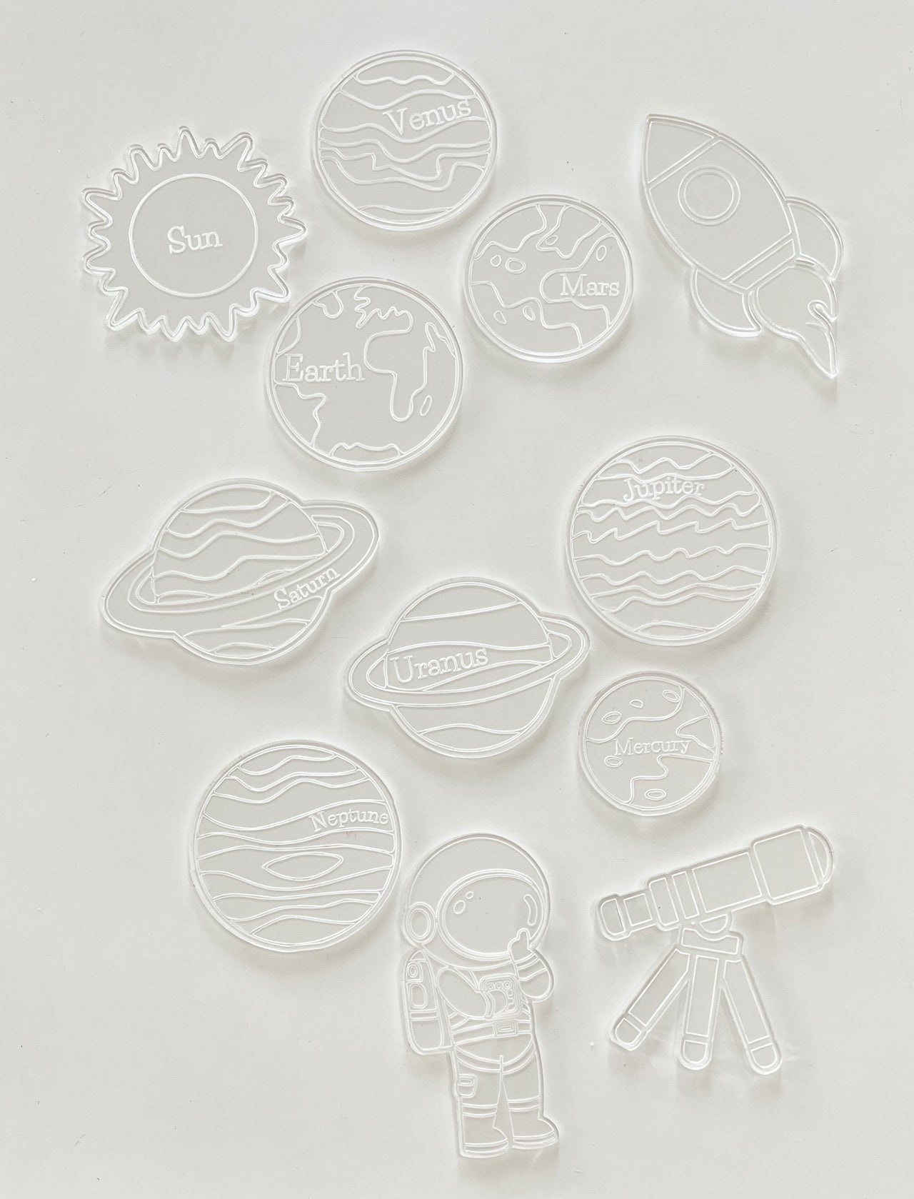 Clear plastic cookie cutters shaped like the sun, planets, an astronaut, rocket, and telescope on white background