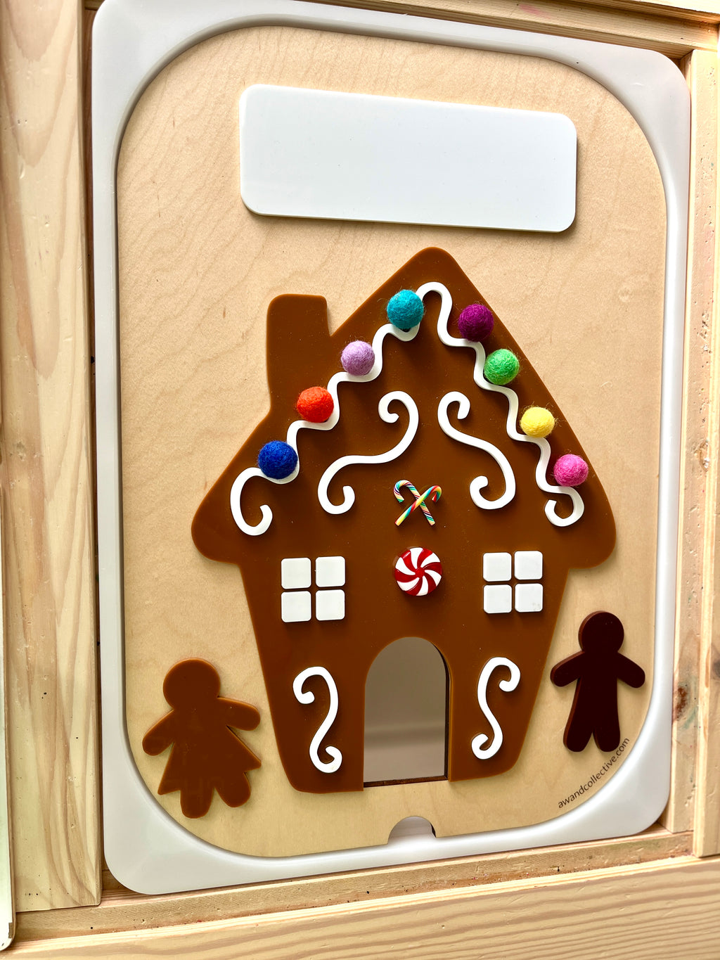 Magnetic wooden gingerbread house with colorful pom-pom decorations and candy cane details on a light wood board