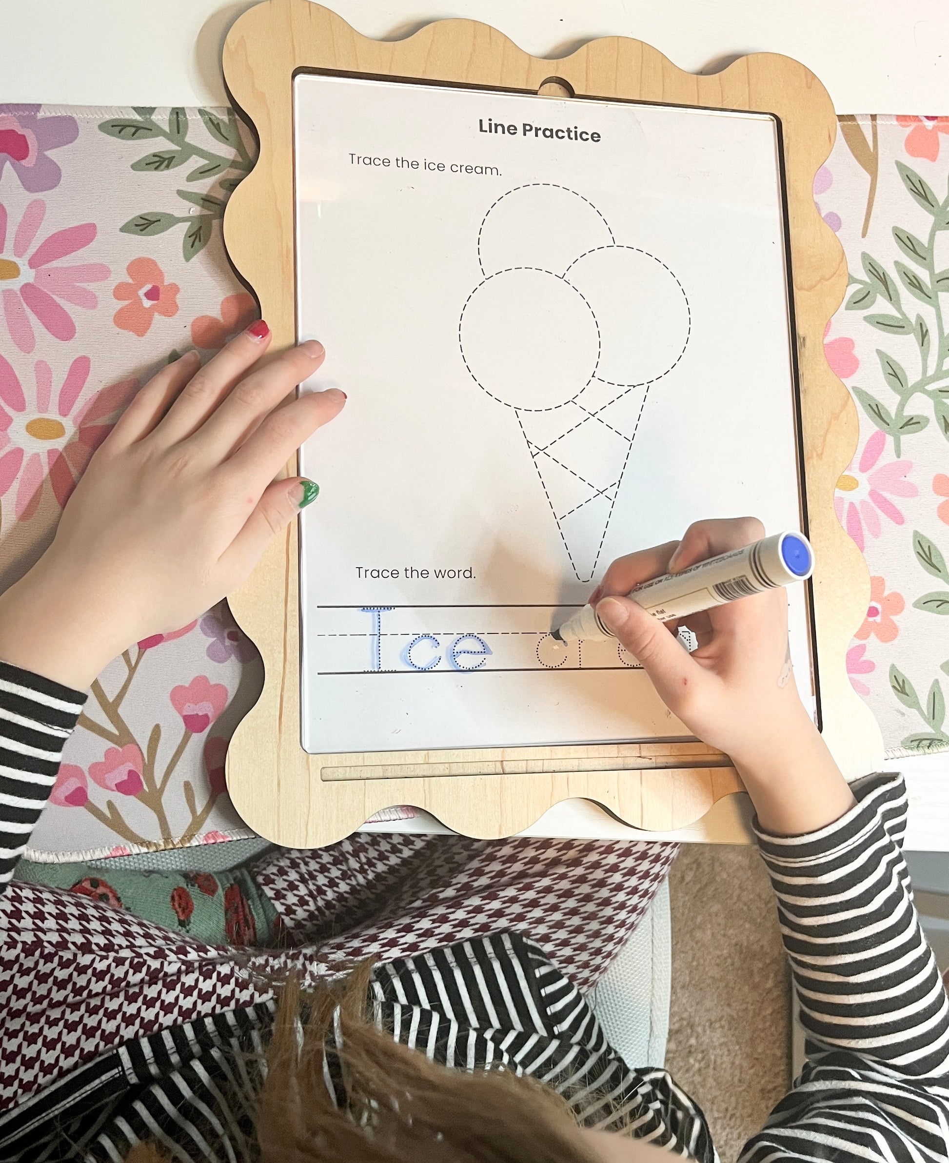 Child tracing an ice cream outline on a educational board with a marker.
