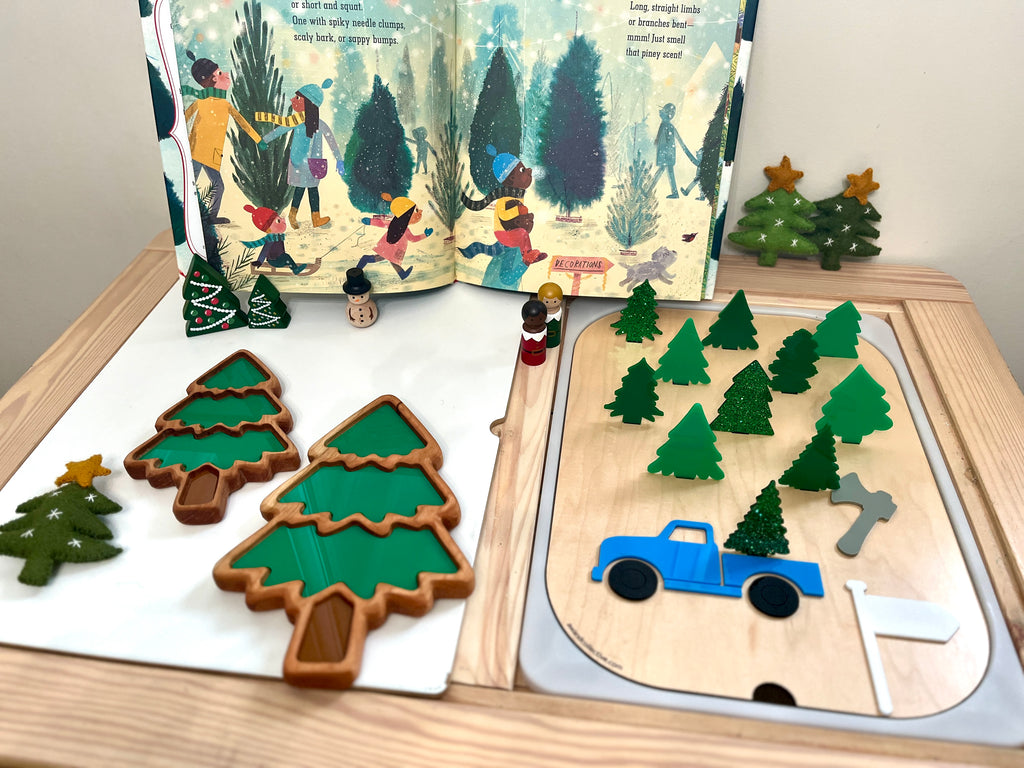 Wooden playset with green Christmas tree shapes, blue truck, gray axe, white flag, and star-topped felt trees on wood surface