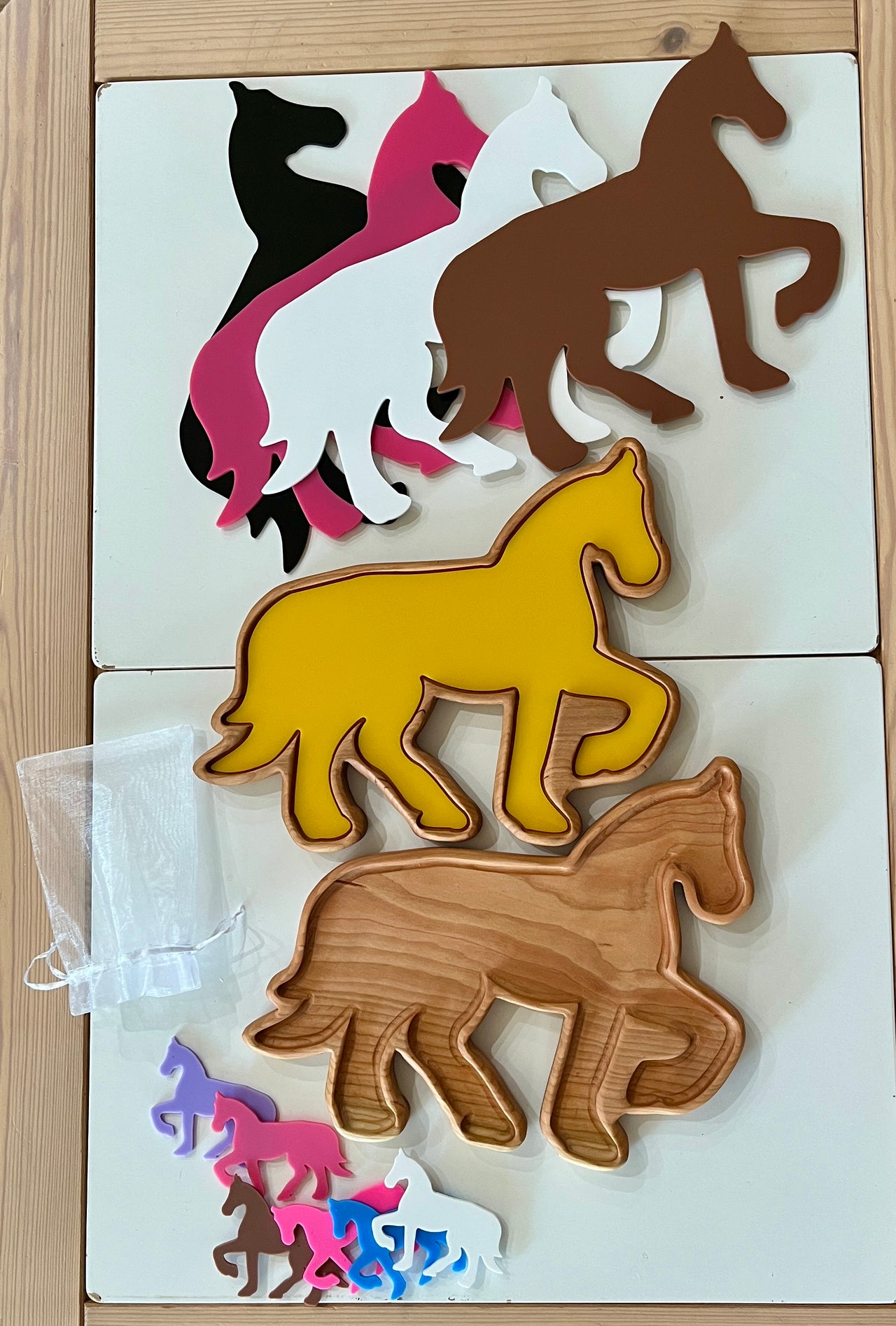 Stack of horse-shaped trays and small cutouts in multiple colors including yellow, brown, black, white, pink, and purple on wooden table