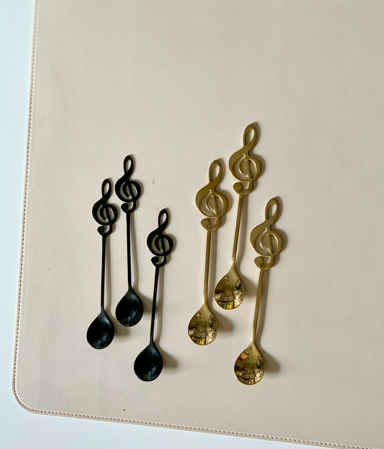 Set of six metal teaspoons with treble clef handles, three in black and three in gold finish, arranged on a light surface