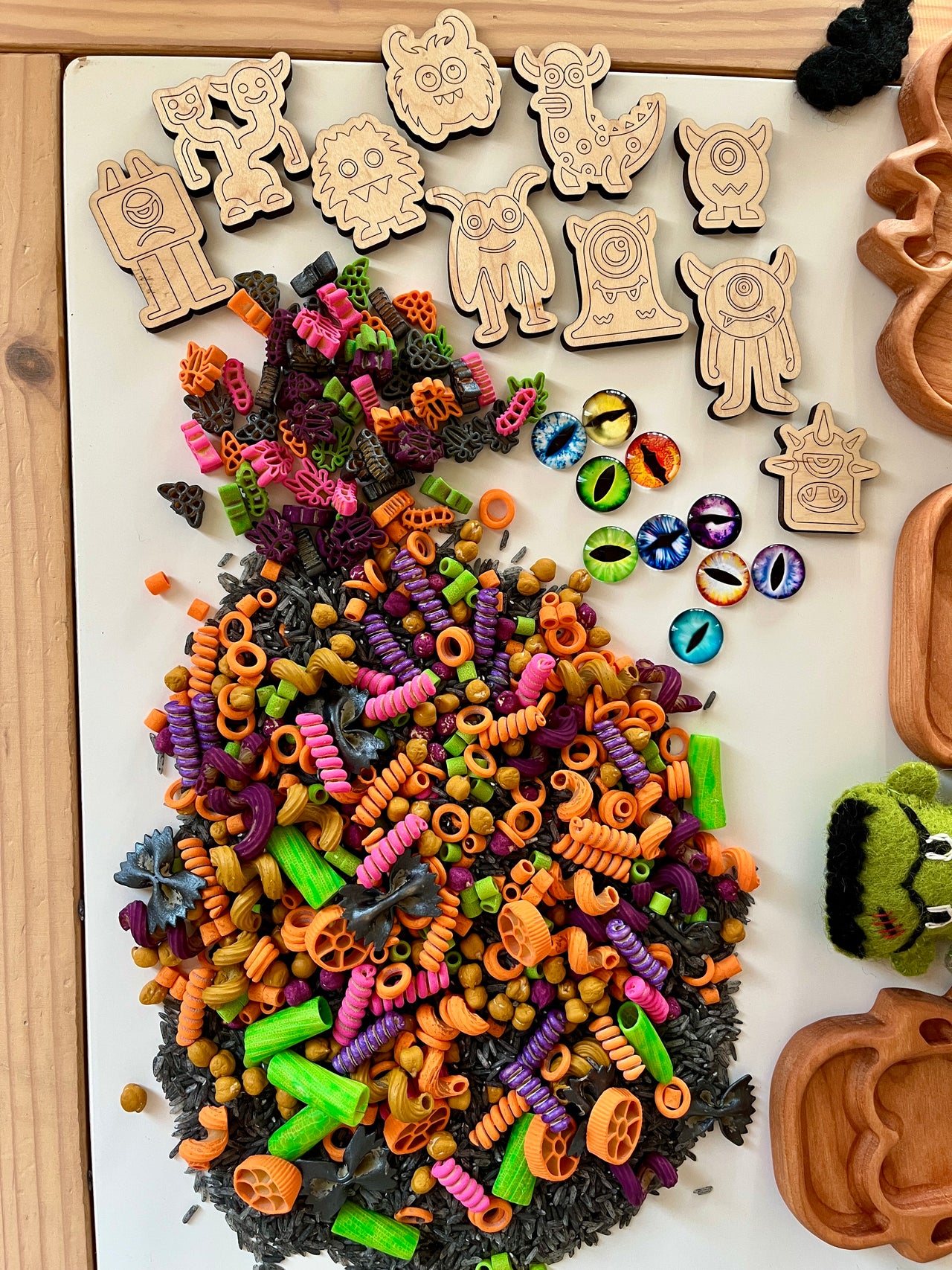 Wooden monster tokens with colorful spiral pasta, plastic monster eye pieces, and wooden trays on light surface