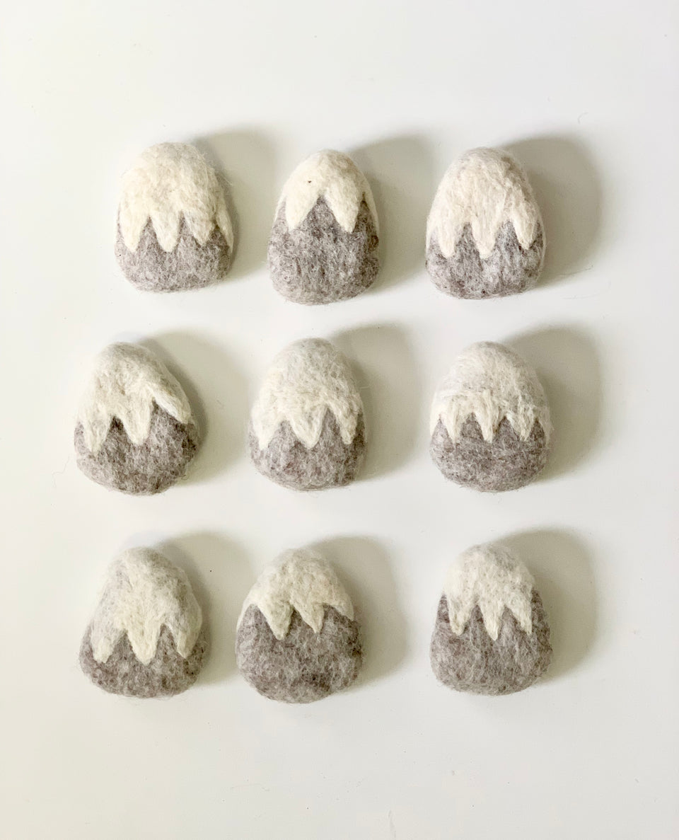 Nine handmade grey felt mountains with white snowy peaks arranged in three rows on white background