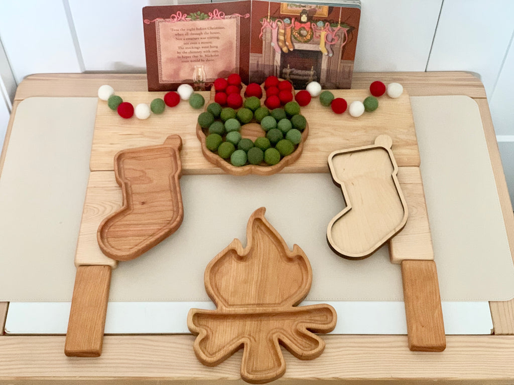 Laser cut wooden stocking and campfire sensory trays with felt balls and holiday garland on wooden table