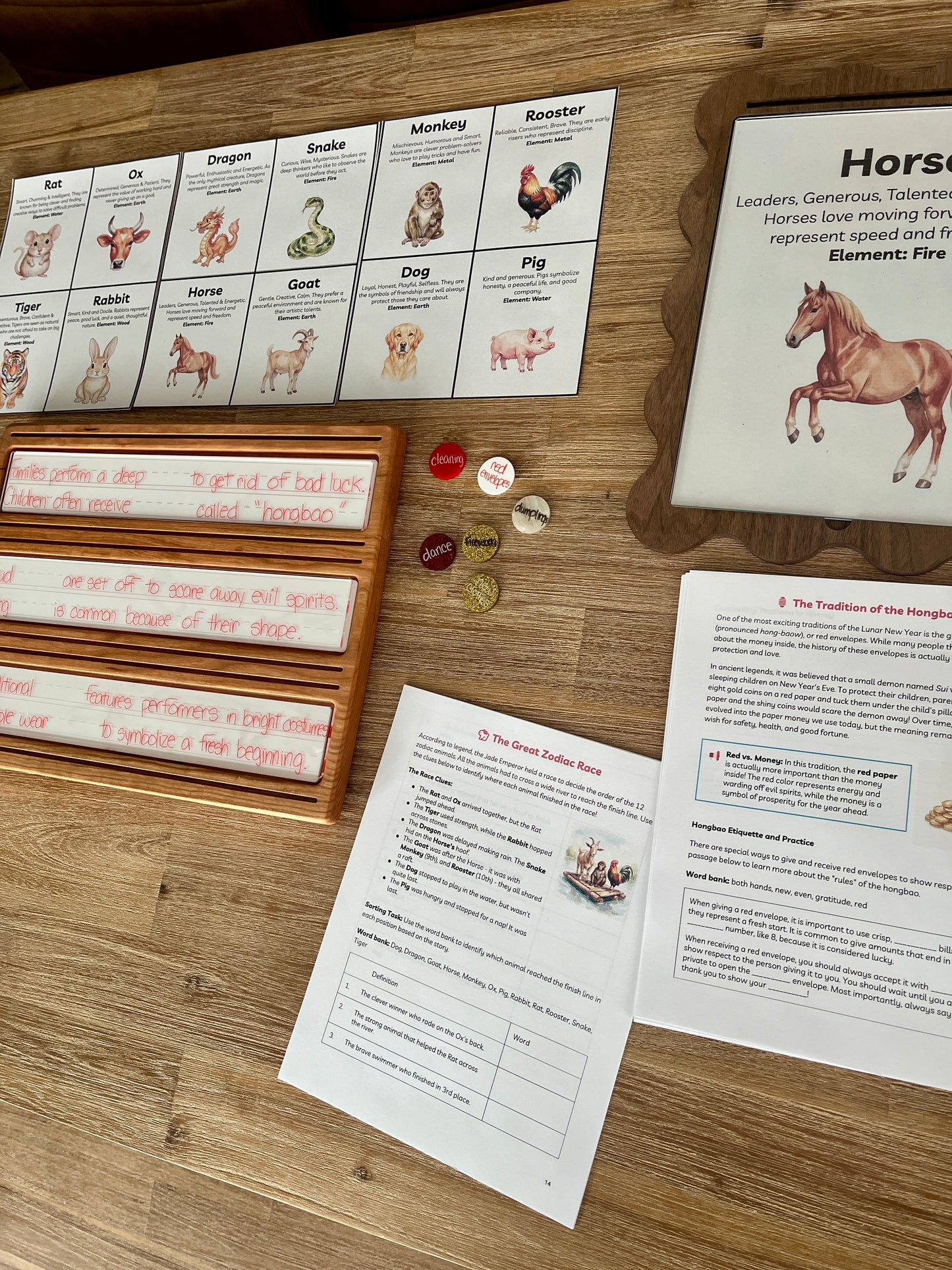 Digital Download | Lunar New Year Unit Study featuring printed learning sheets with zodiac animal illustrations, wooden trays holding dry erase marker practice, and small round sensory fillers, handcrafted homeschool education resources.