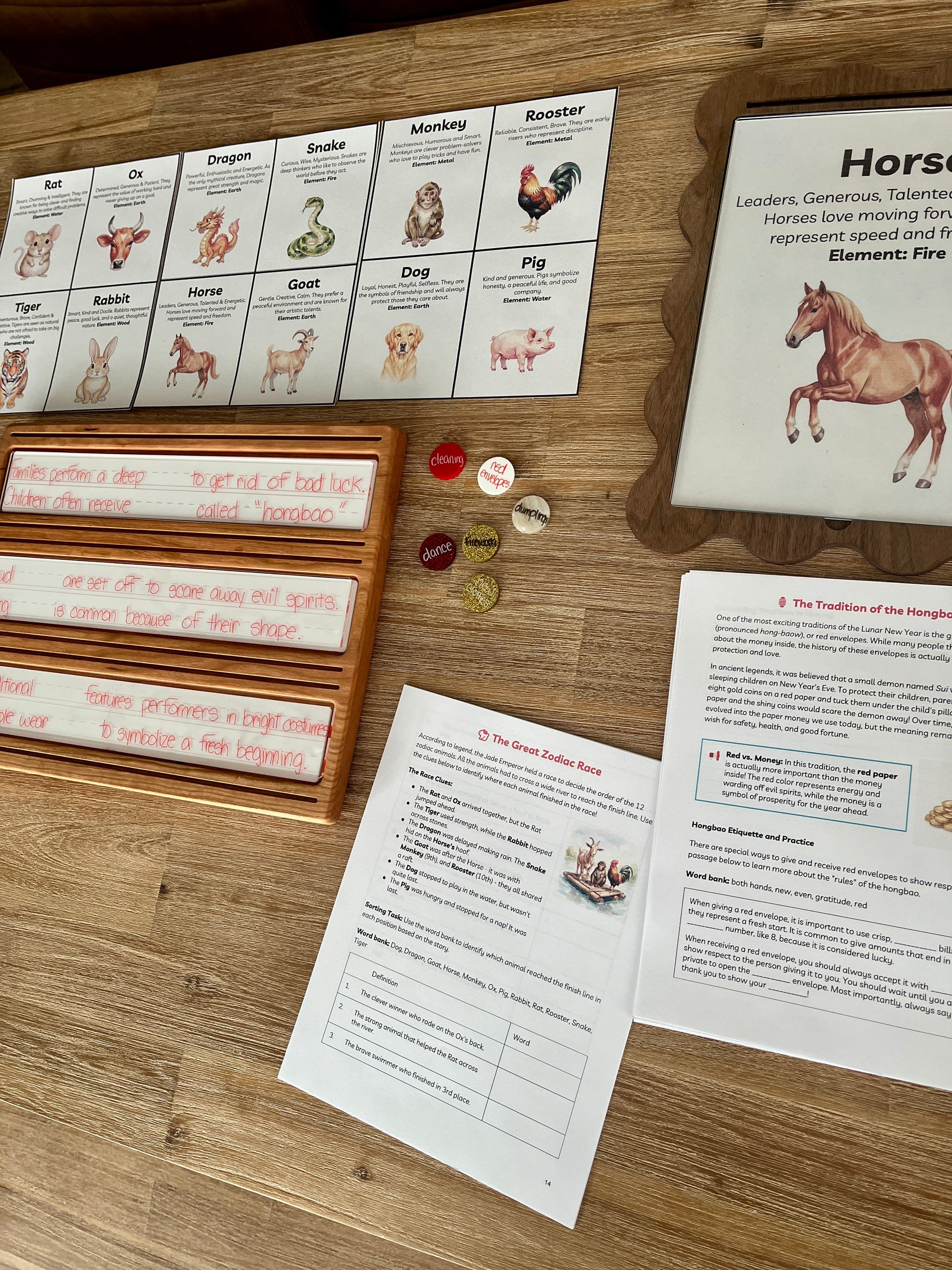 Digital Download | Lunar New Year Unit Study featuring printed learning sheets with zodiac animal illustrations, wooden trays holding dry erase marker practice, and small round sensory fillers, handcrafted homeschool education resources.