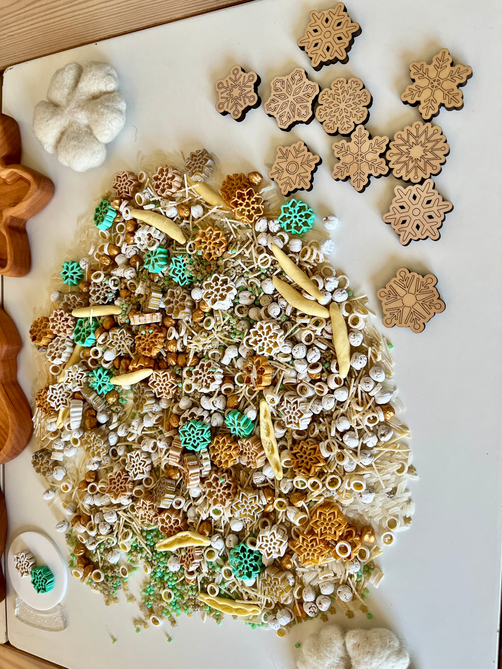 Assortment of wooden snowflake shapes and various textured natural sensory materials scattered on white surface