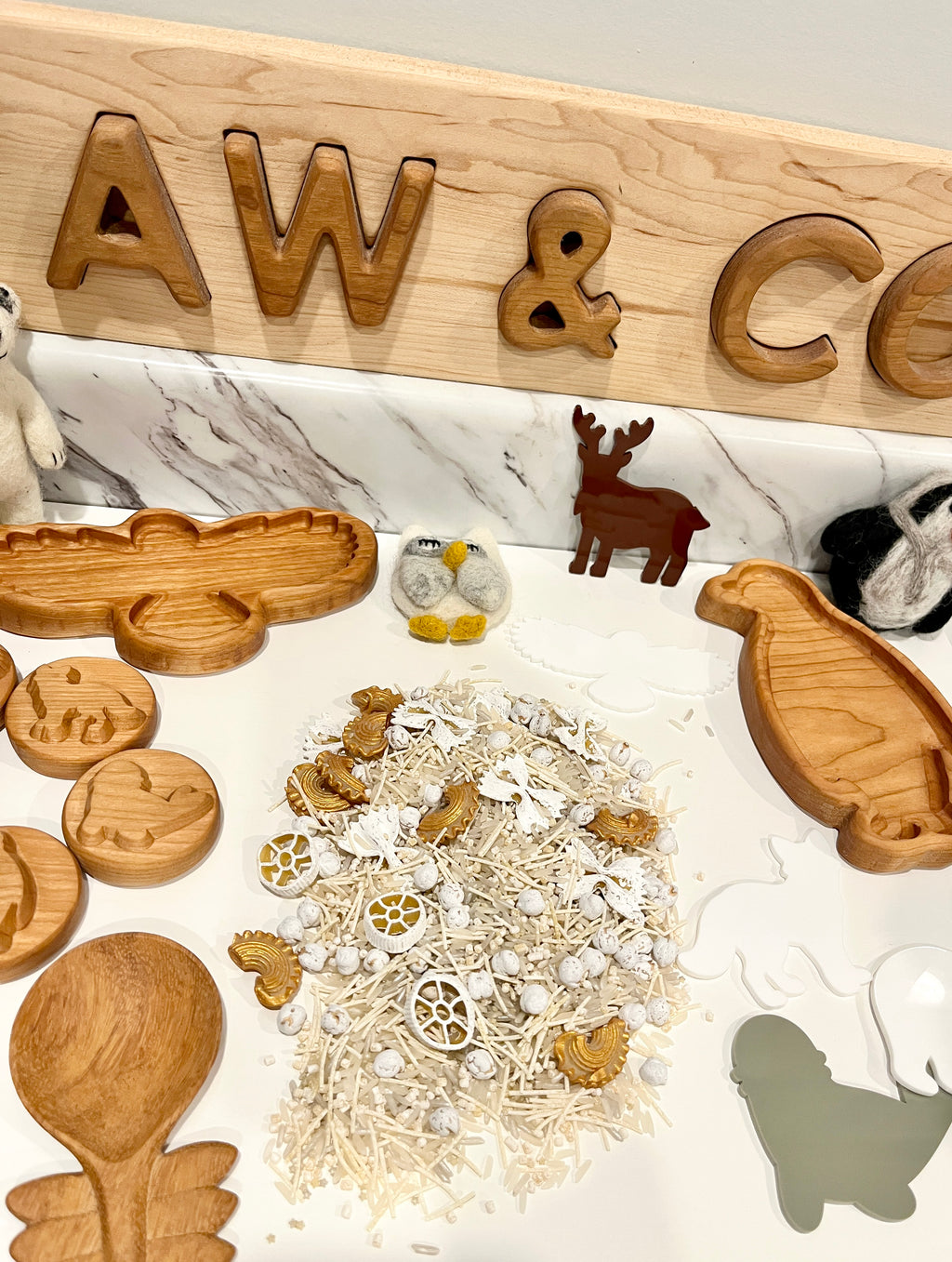 Arrangement of wooden animal-shaped trays, small textured balls, and felt animal figures on white marble surface