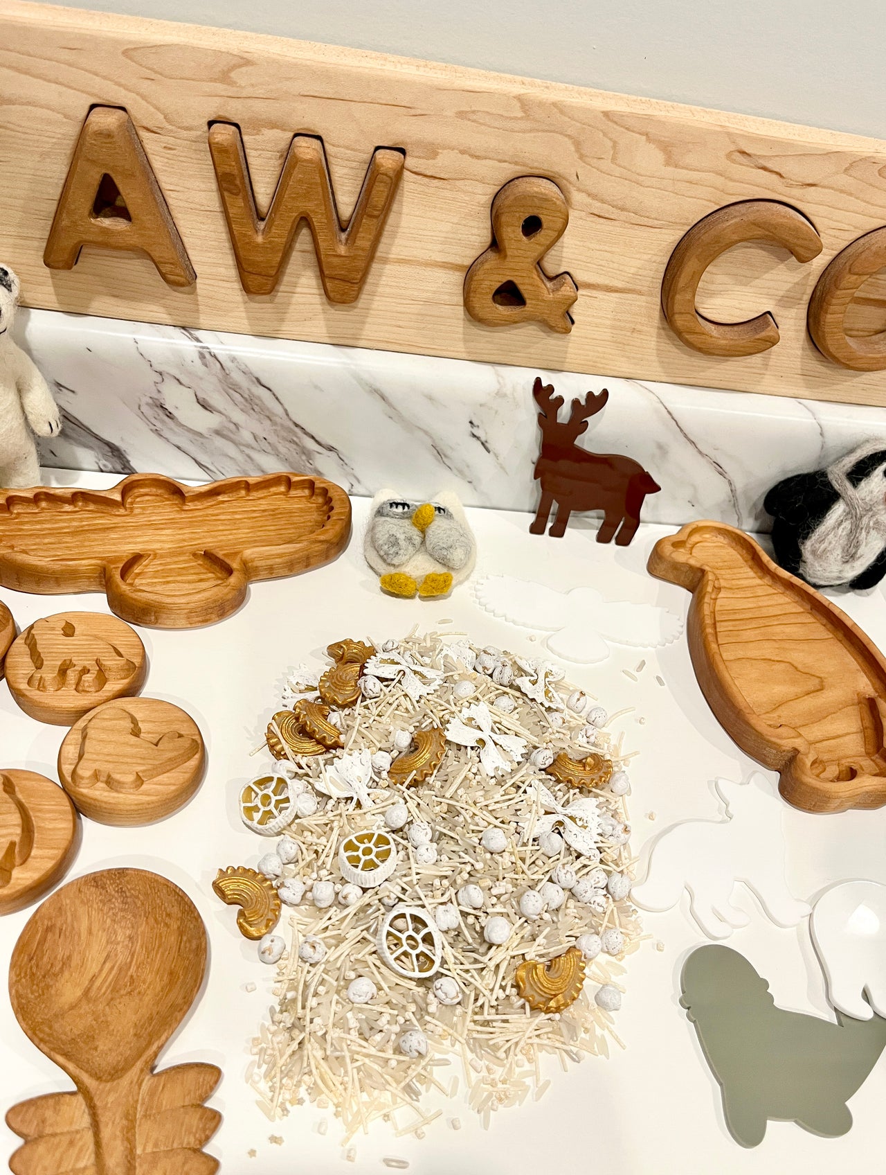 Arrangement of wooden animal-shaped trays, small textured balls, and felt animal figures on white marble surface