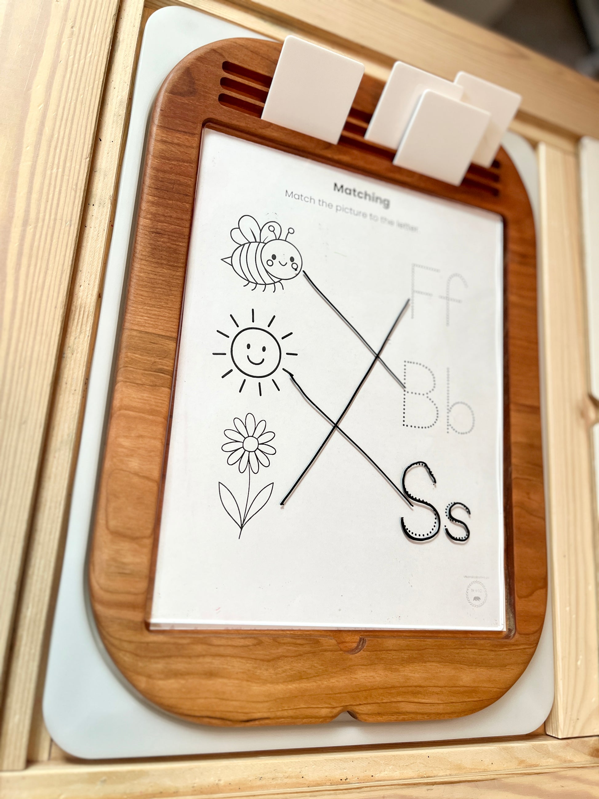Wooden educational tray with dry erase insert with a paper displaying letters and shapes