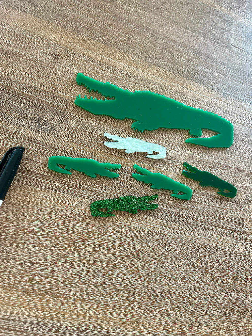Little Dry Erasables - Crocodiles featuring handcrafted green and white crocodile shapes in various sizes made from wood and acrylic, displayed on a wooden surface with a black marker, homeschool educational resources.