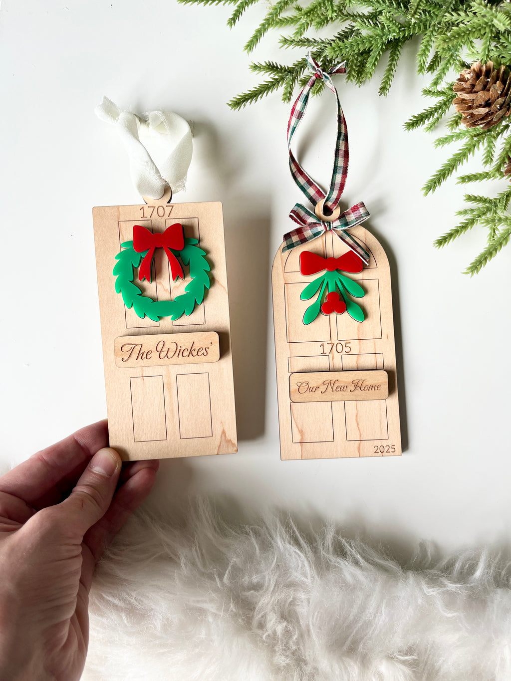 Two wooden door-shaped Christmas ornaments with festive greenery, red bows, and personalized name plaques on ribbons