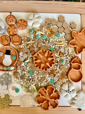 Wooden trays and felt shapes with snowflakes, beads, and winter-themed miniature decorations on a white surface