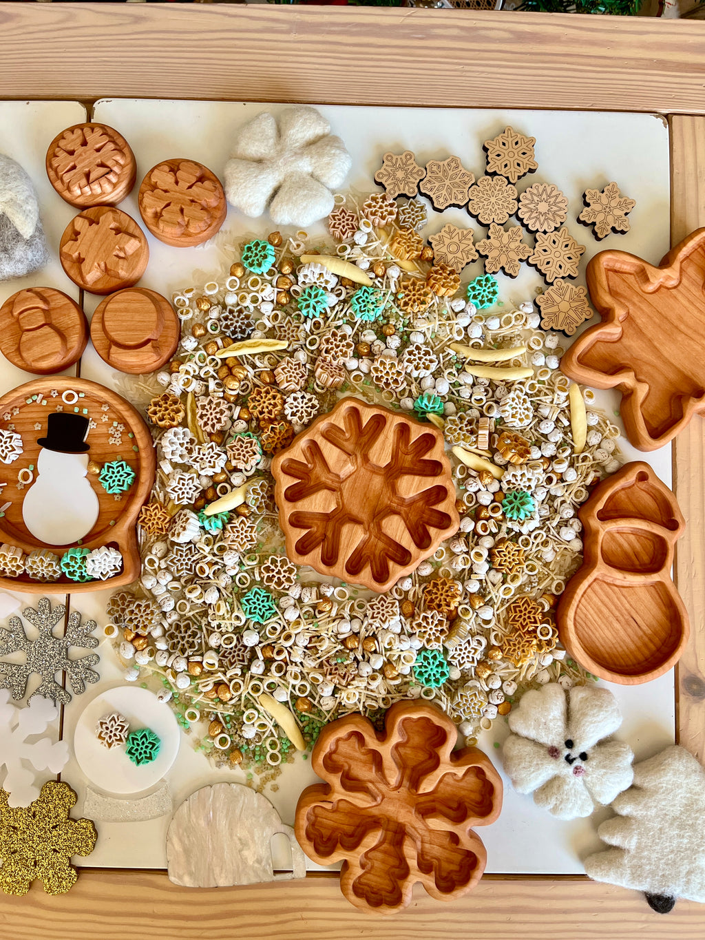 Wooden trays and felt shapes with snowflakes, beads, and winter-themed miniature decorations on a white surface