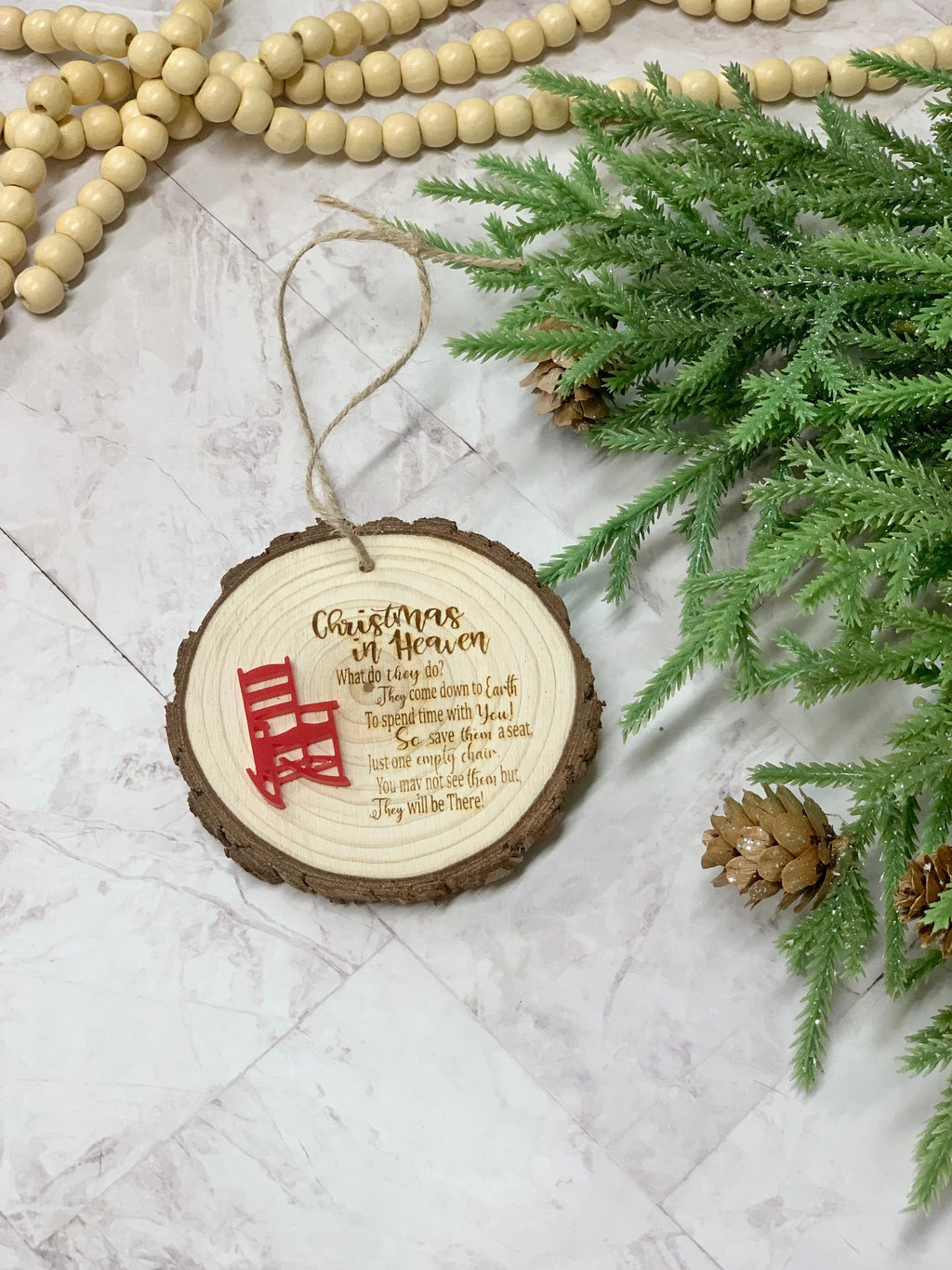 Wood slice Christmas ornament with memorial poem and small red rocking chair detail on white marble surface with greenery