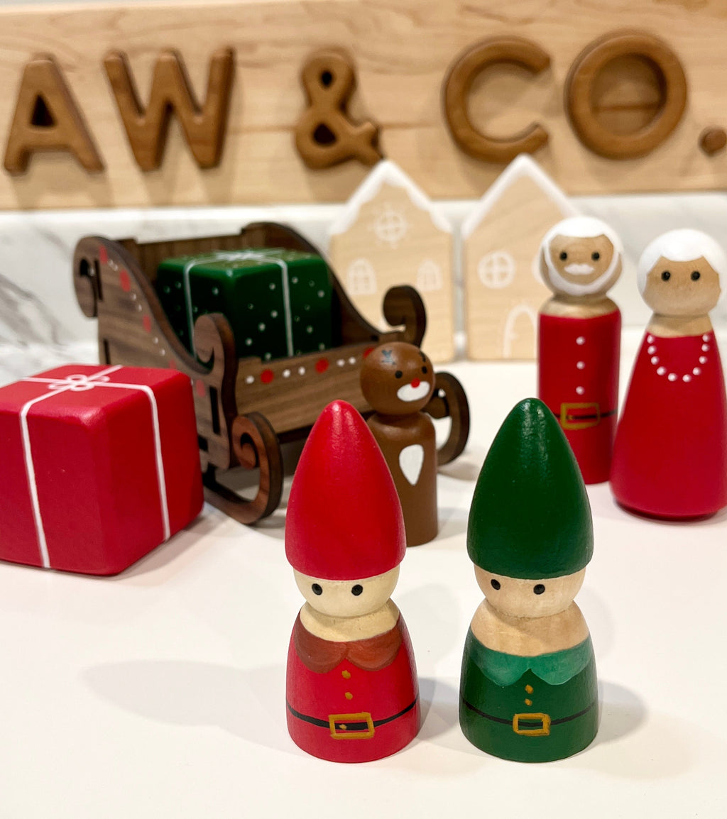Wooden figurines including two elves, Santa, gingerbread man, sleigh with presents, and festive house cutouts
