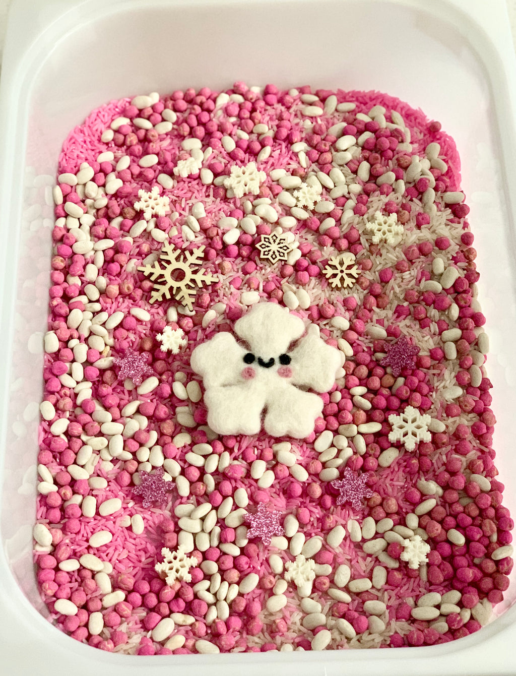 Pink snowflake sensory kit with pink filler, white beans, wooden snowflakes, and felt snowflake figure in white tray