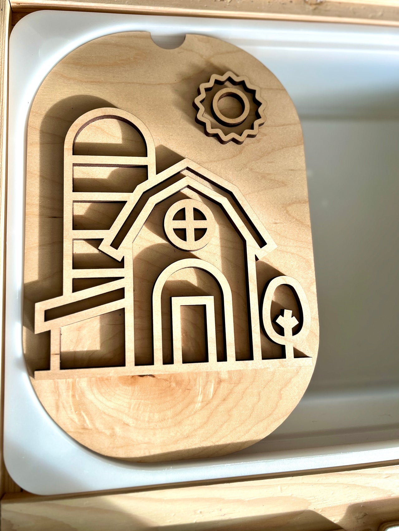 Light wooden puzzle board featuring a barn, silo, tree, and sun cutout shapes on a light surface