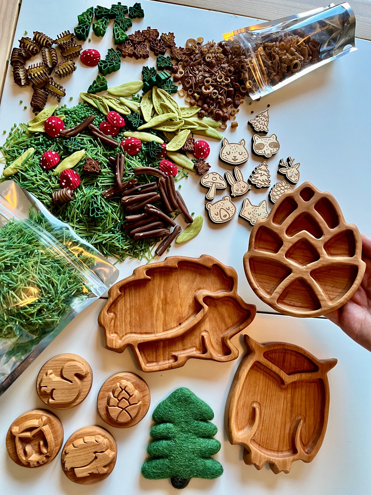 Set of three wooden divided trays shaped like a pinecone, hedgehog, and owl with woodland-themed loose parts on white surface