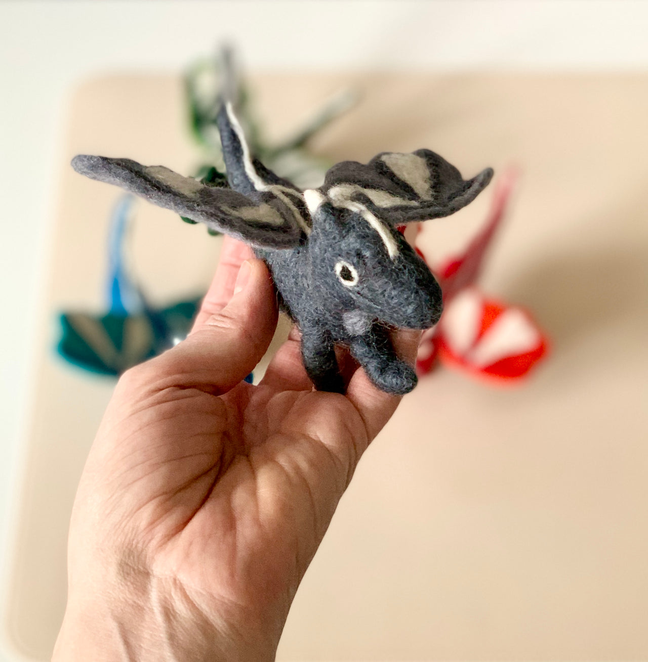 Hand-stitched dark gray felt dragon toy with white accents held in hand with colorful felt dragons blurred in background