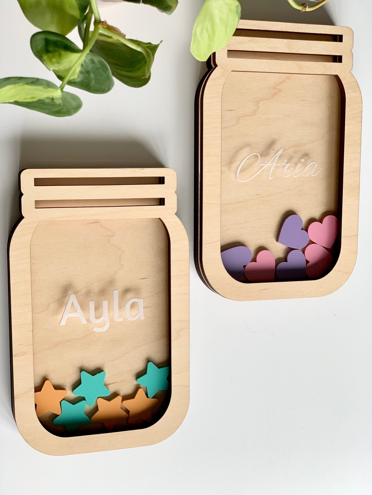 Two wooden jar-shaped frames with the names Ayla and Aria, filled with colorful star and heart tokens on a white surface