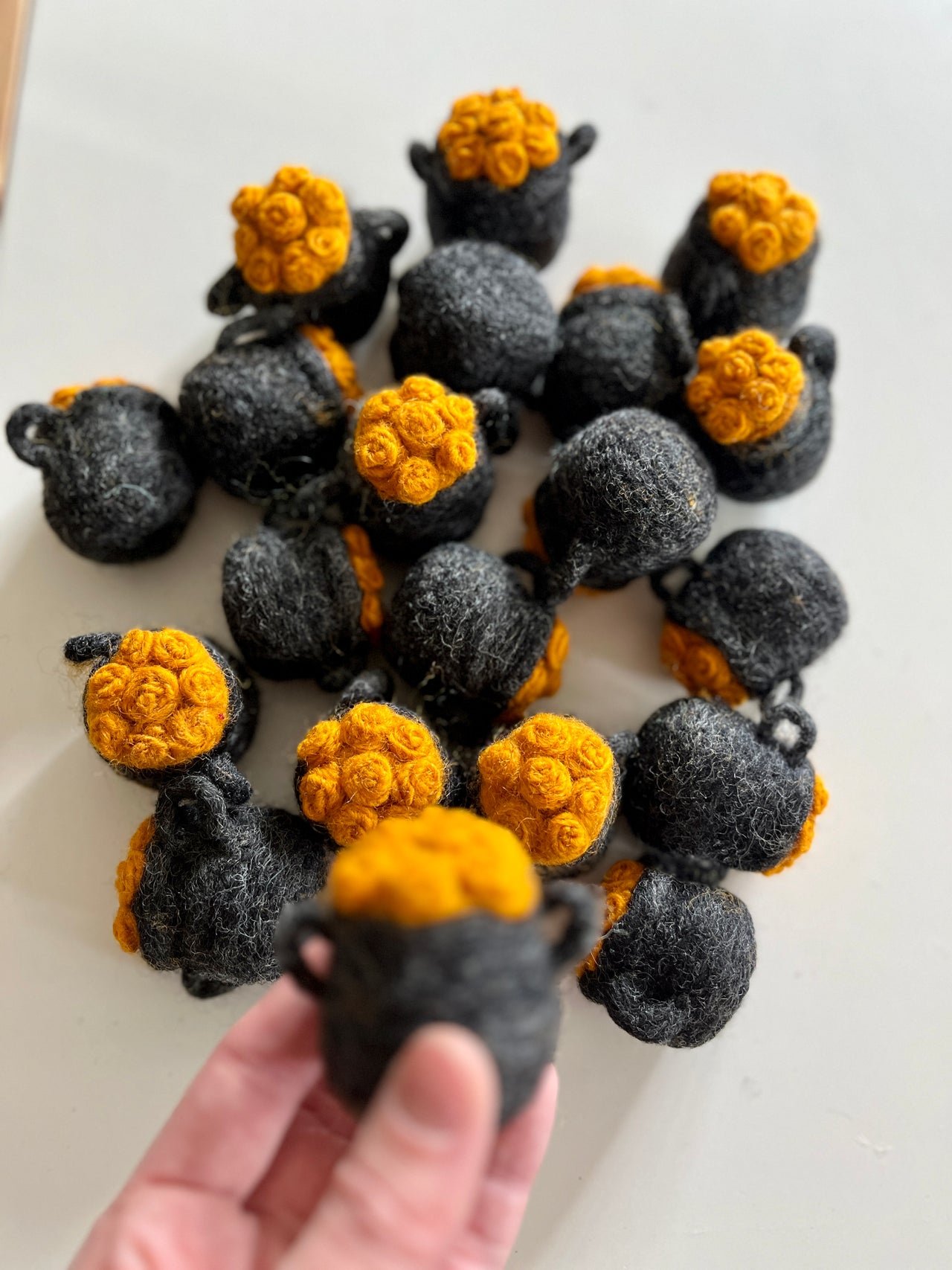 Hand holding small black felt pots topped with bright yellow rosette clusters scattered on white surface