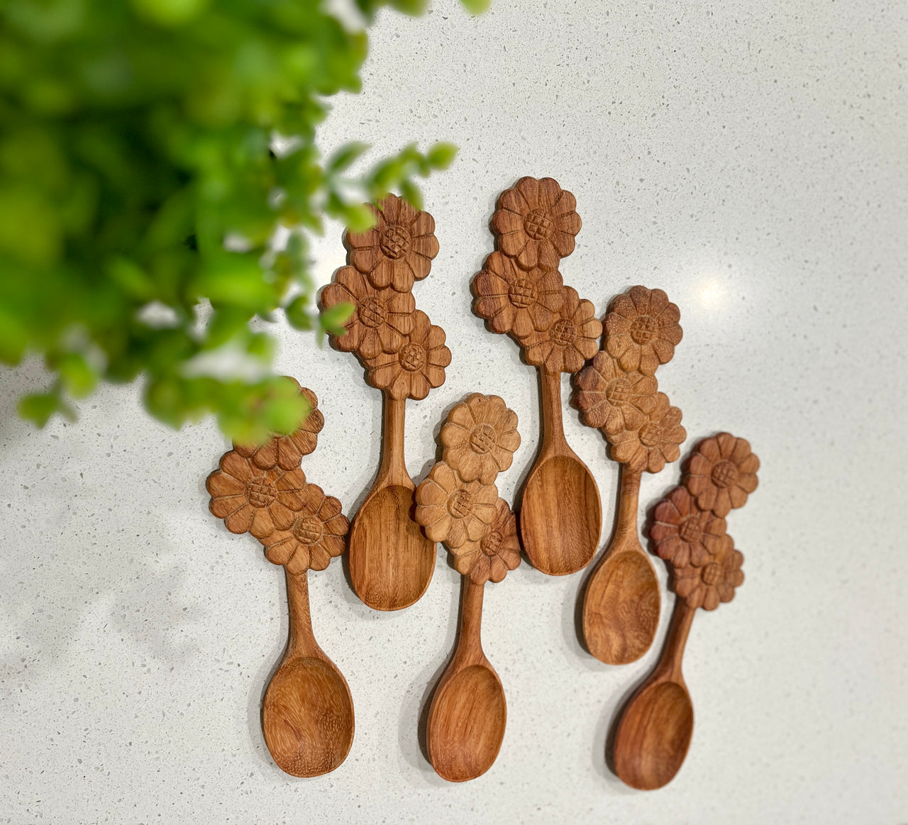 Set of six wooden spoons with intricately carved floral designs on the handles arranged on a white surface