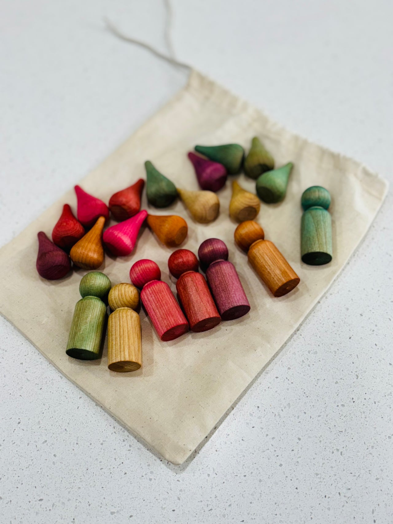 Collection of colorful wooden peg dolls and cone-shaped pieces arranged on a natural fabric drawstring bag