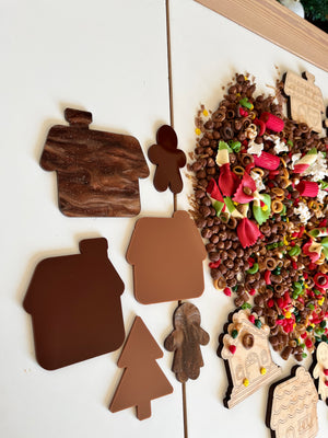 Assorted brown house and holiday-themed cutouts arranged next to colorful pasta and grain sensory materials on white surface