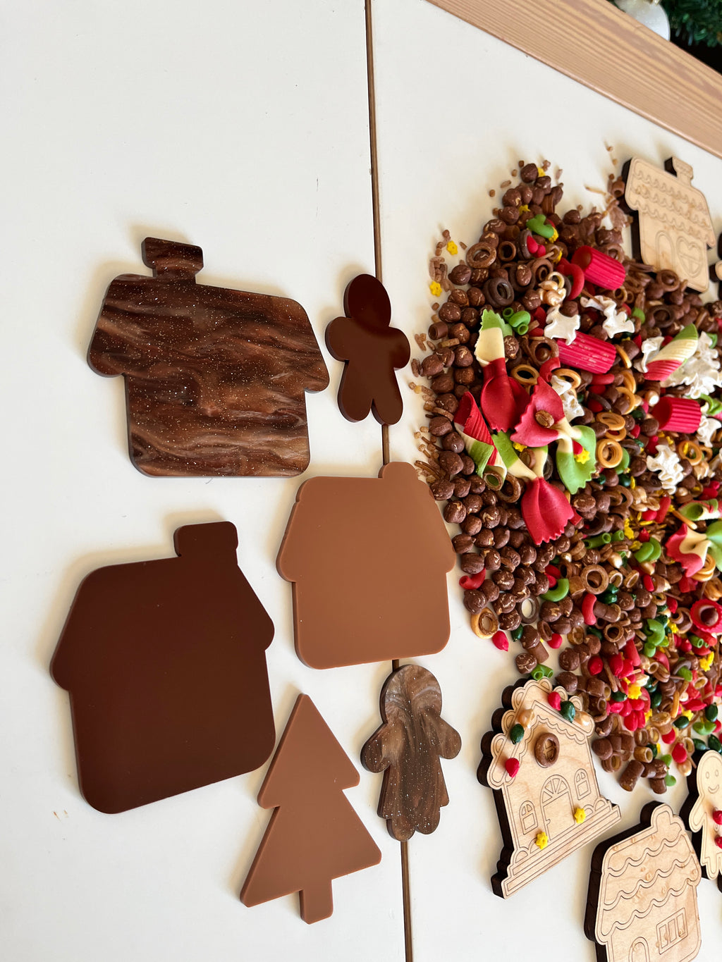 Assorted brown house and holiday-themed cutouts arranged next to colorful pasta and grain sensory materials on white surface