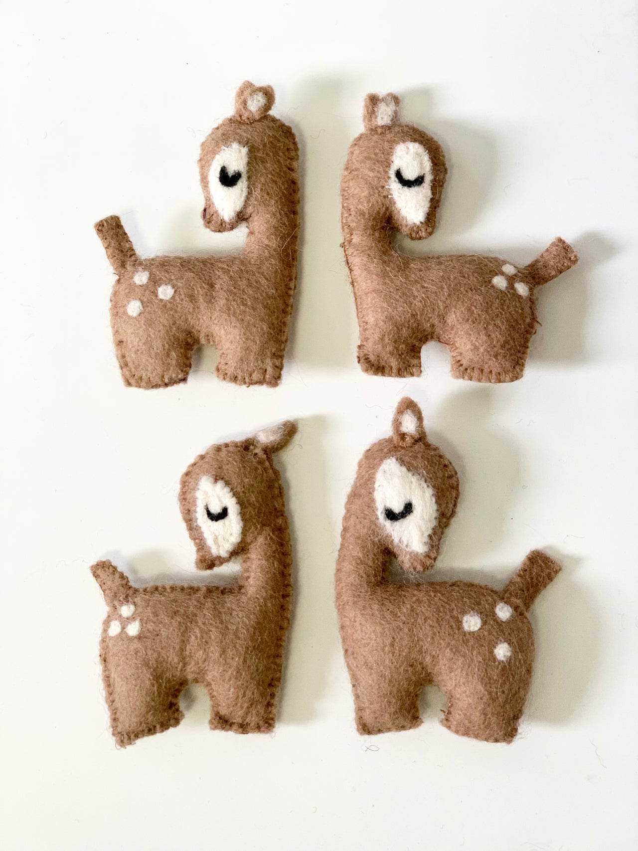 Set of four handmade felt deer figures with stitched details in brown and white on white background