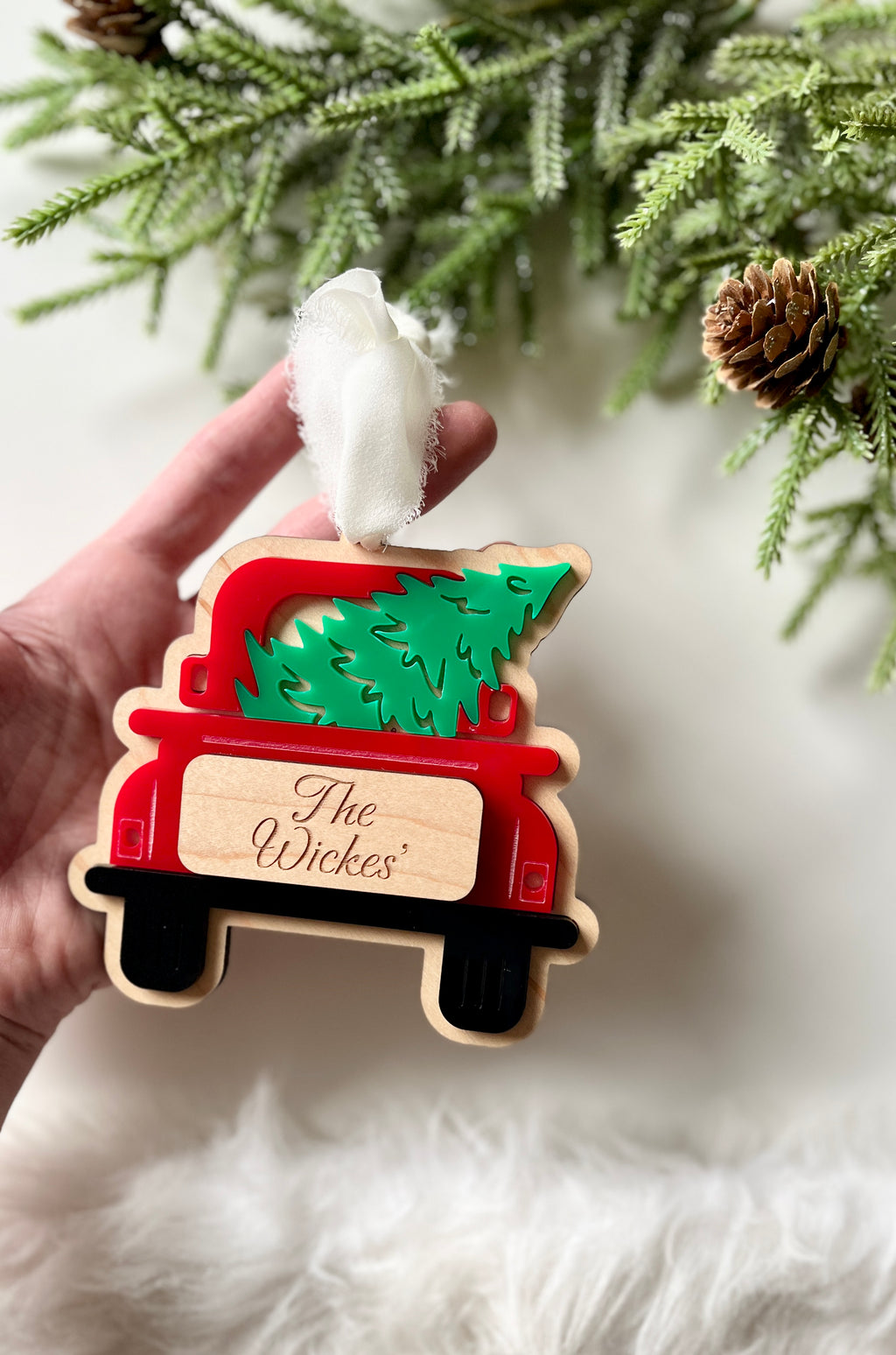 Hand holding wooden Christmas ornament shaped like red truck carrying green tree with personalized name tag